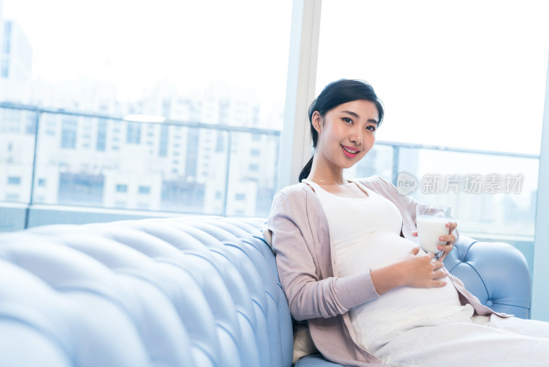 年轻孕妇在沙发上喝牛奶
