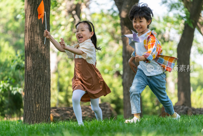 两个小孩子在草地上举着风车开心奔跑