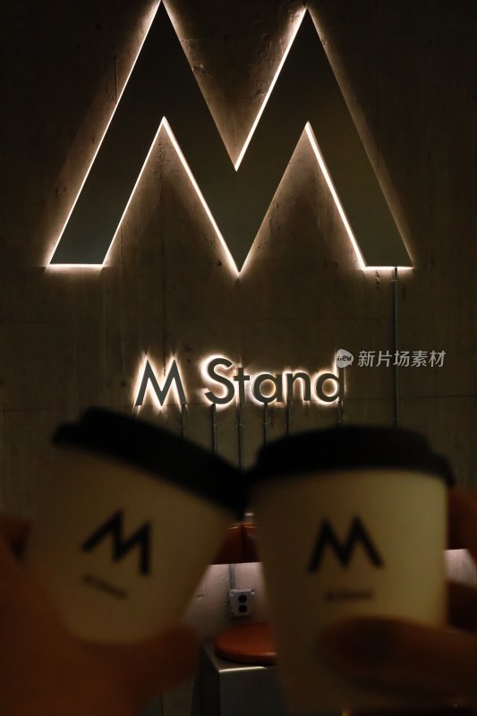 手拿咖啡杯与M Stand标志合影