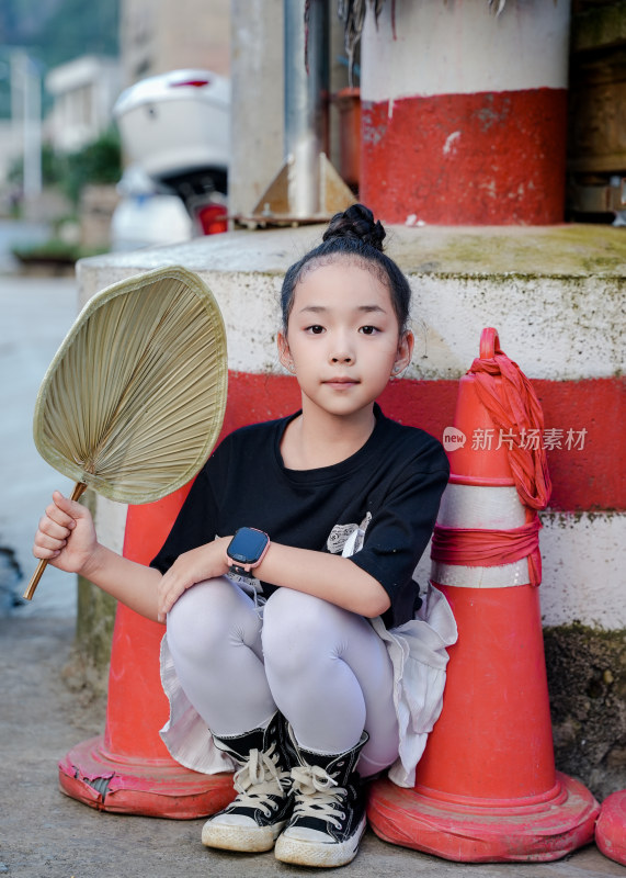 小女孩手持蒲扇蹲在交通锥旁