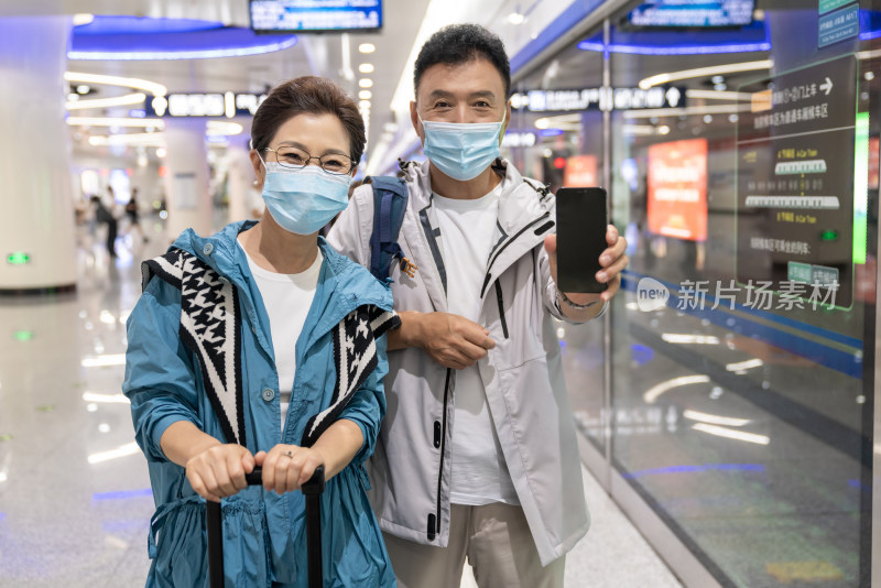 快乐的老年夫妇在地铁戴着口罩展示手机