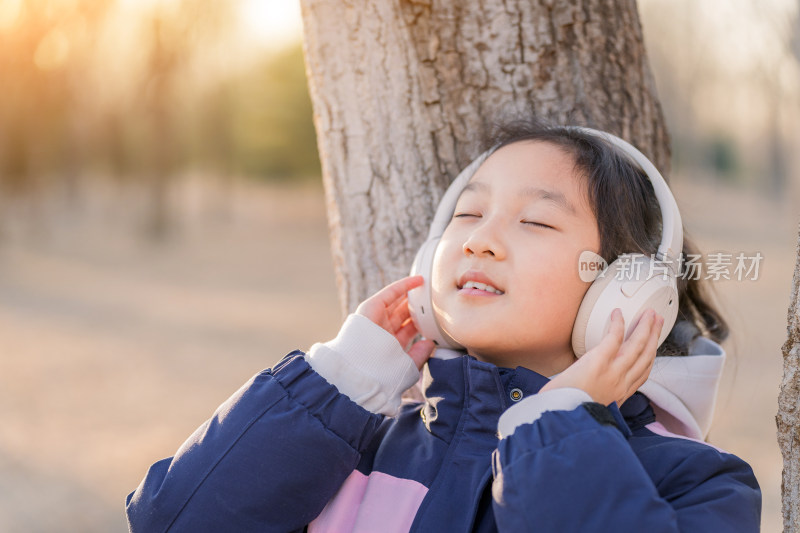 冬日暖阳在公园树林中带耳机欣赏音乐的女孩