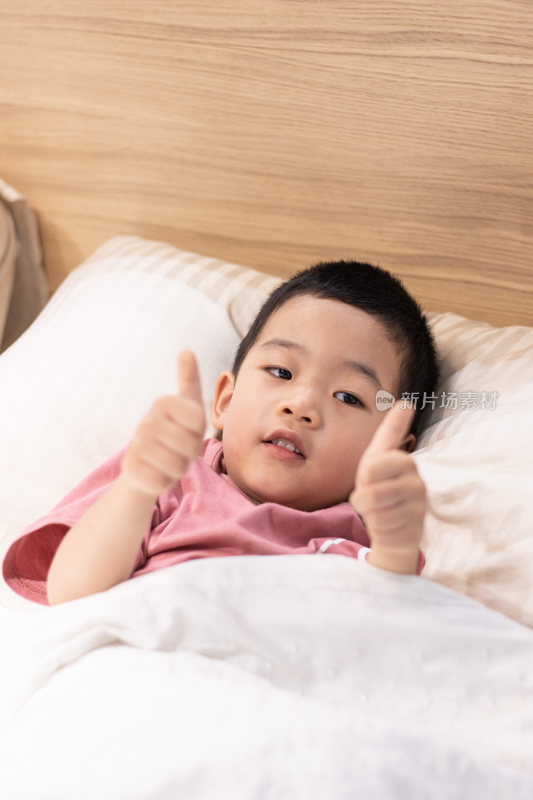 一个小男孩躺在舒适的床上竖大拇指