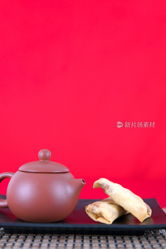 红背景上盘子里的炸春卷和一壶茶