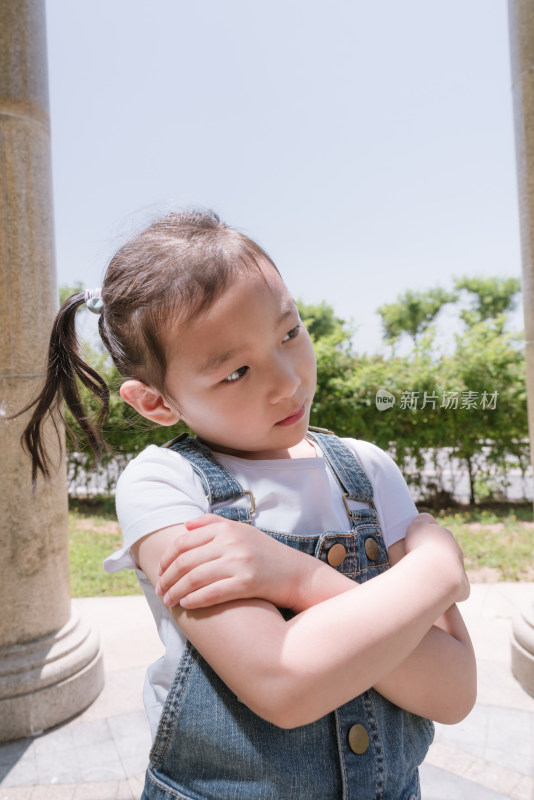 穿背带裤小女孩户外双臂交叉站立