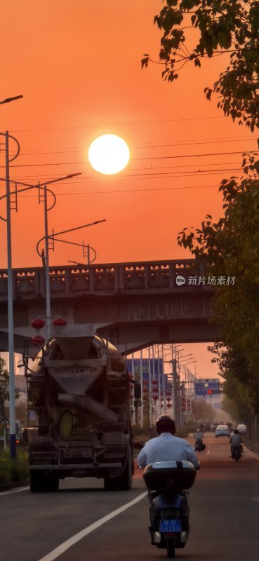 夕阳下的公路上有卡车和骑摩托的人