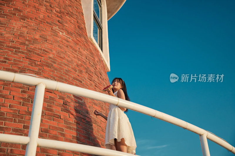 盛夏夕阳湖边码头灯塔上吃西瓜的少女