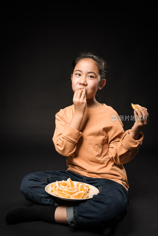 坐在黑背景前吃水果的亚裔女孩