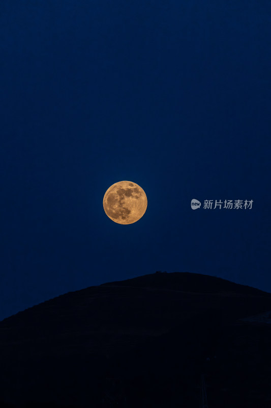 深蓝色夜空下山巅之上的金色满月