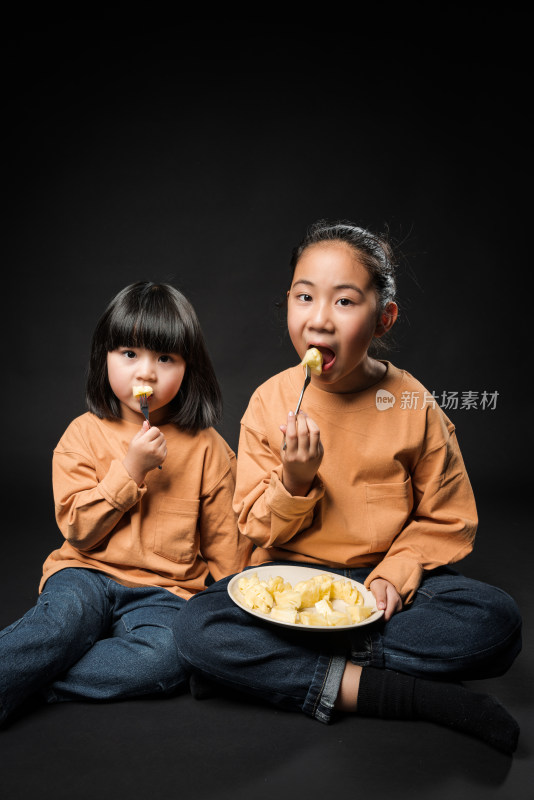 坐在黑背景前吃水果的两个亚裔女孩