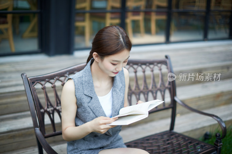 院子里坐在长椅上阅读书籍的亚洲长发少女