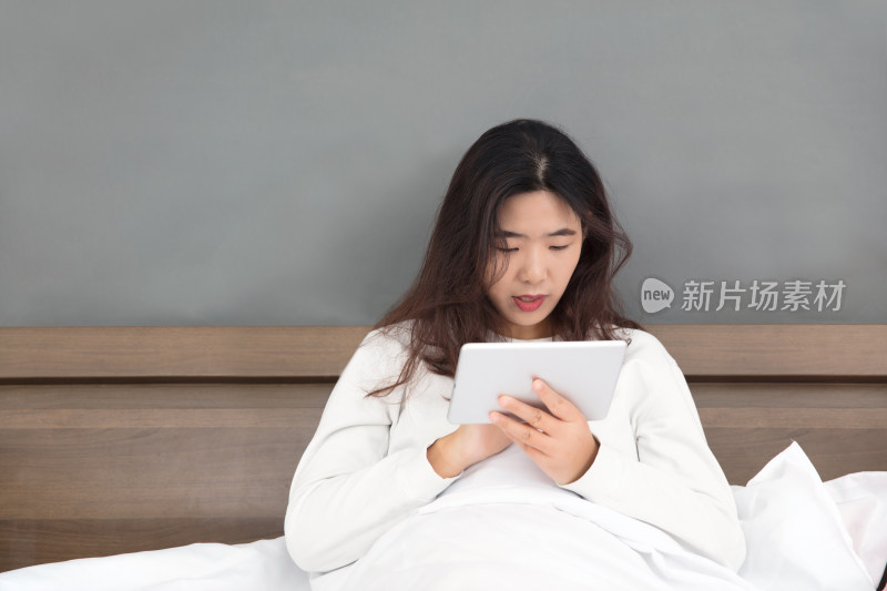 假期懒散的女性坐在床上看iPad