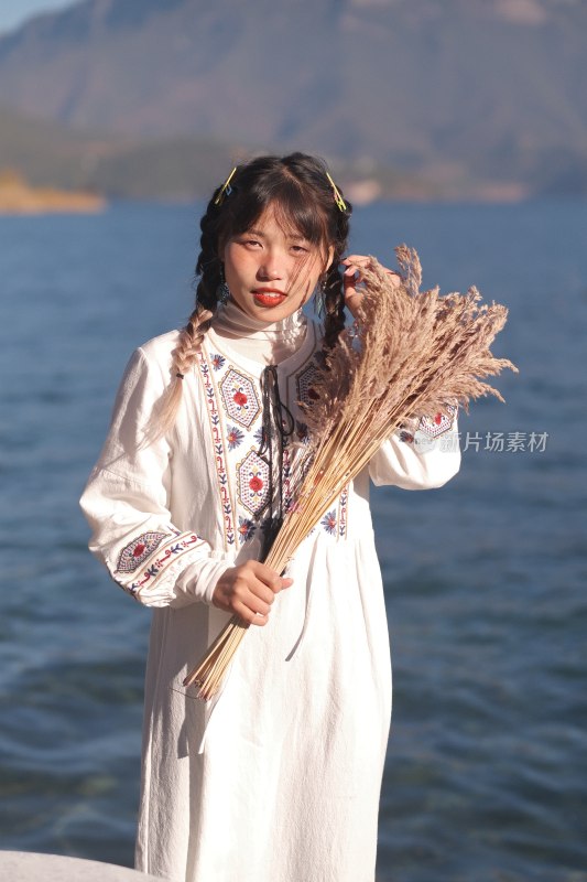 温暖阳光下捧着芦苇站在湖边的温柔女子