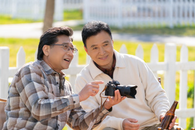 两个老年男人坐在露营地看数码相机