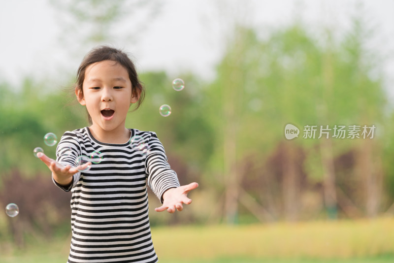 在草坪上玩吹泡泡游戏的女孩