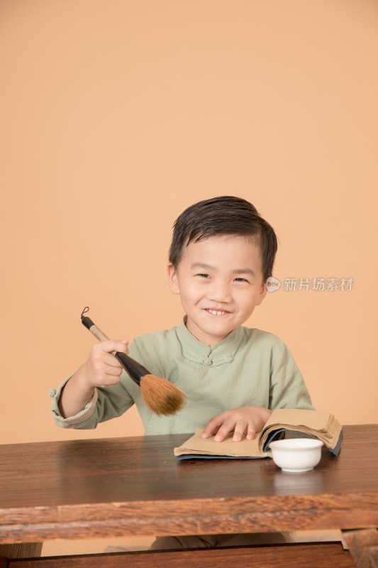 拿着毛笔坐在书桌前的中国古风小男孩