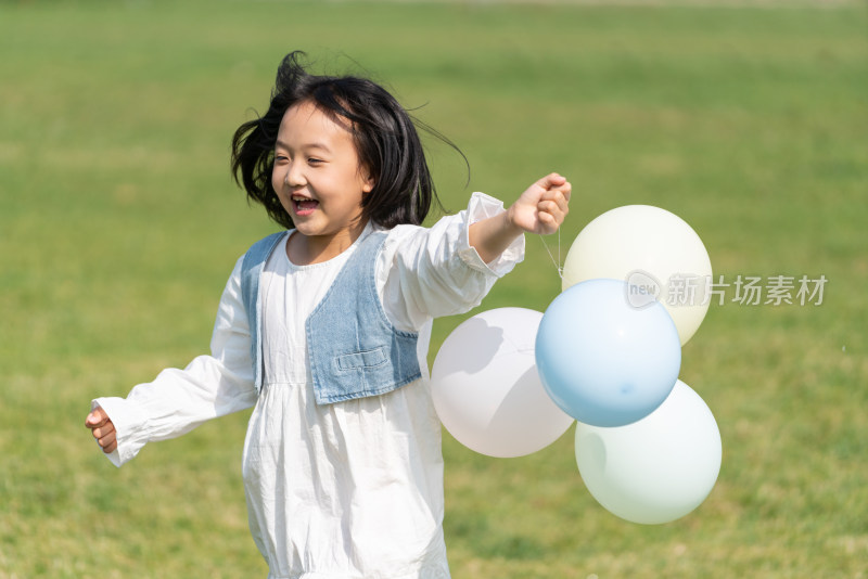 一个小女孩在草地上拿着气球奔跑