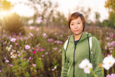 年轻的中国籍女性站在公园的花丛前