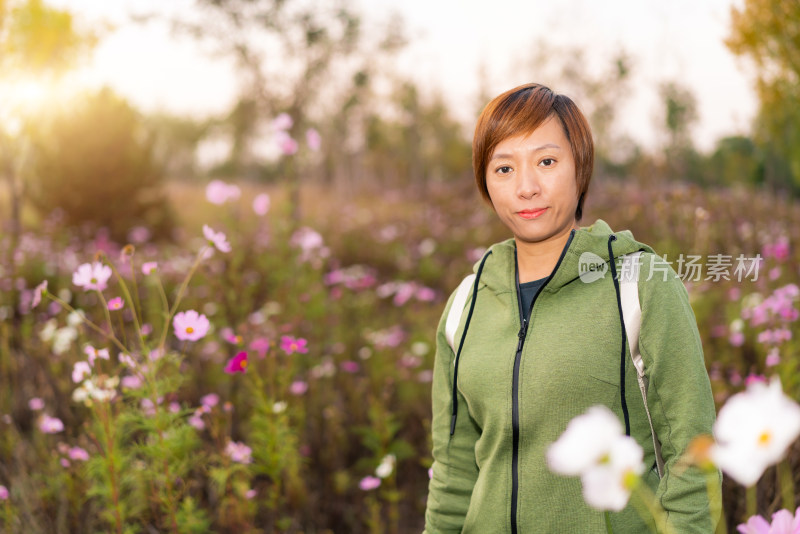 年轻的中国籍女性站在公园的花丛前