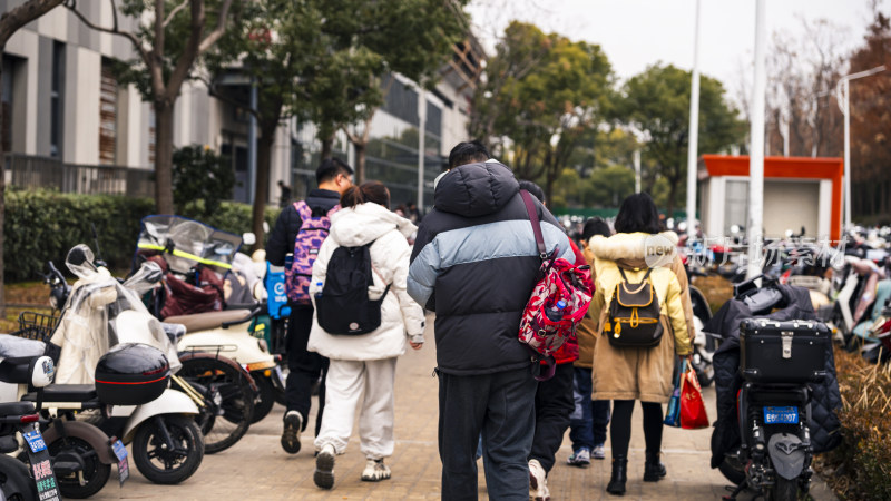 人们背着包走在停放着电动车的人行道上