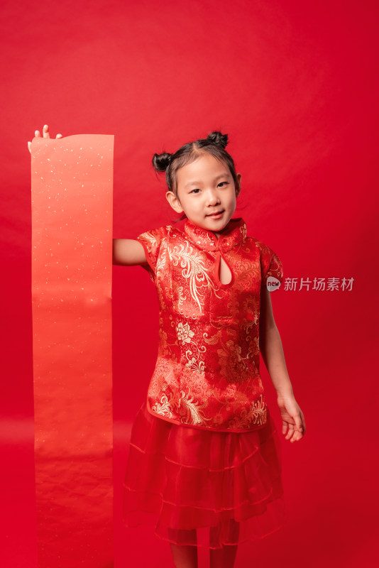 红色背景前穿旗袍拿空白春联纸的中国女孩