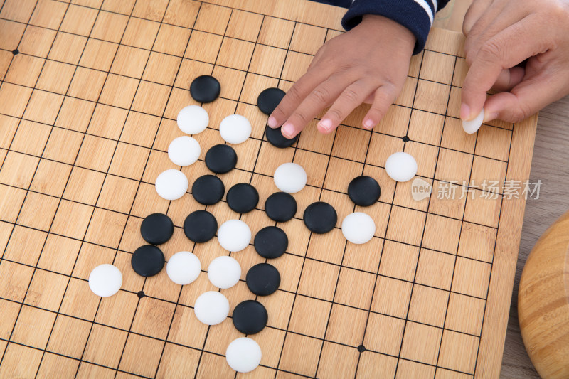 一只大人的手指导着小孩的手下围棋