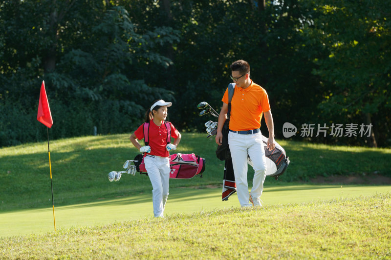 球场上教练和学生背着高尔夫球包行走