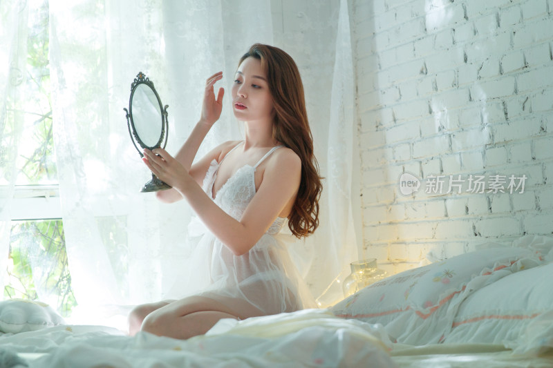漂亮的青年女人坐在床上照镜子