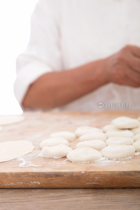 砧板上散落着小面团和背景里正在包饺子的手