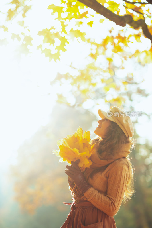 女子手持秋叶于秋日树林中