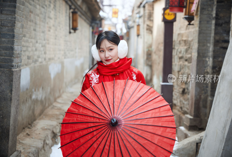 雪后在老城古巷穿着喜庆服饰的亚洲少女