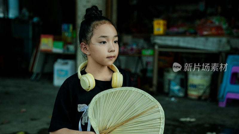 手持折扇戴耳机的小女孩室内近景照