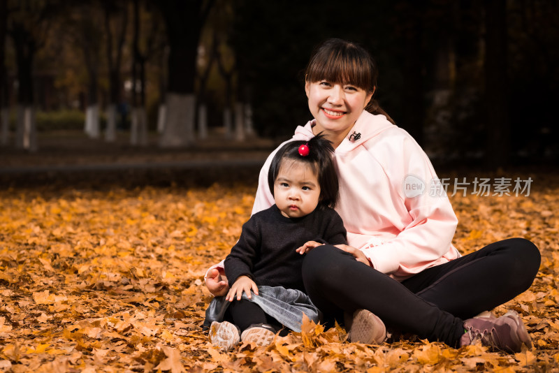 深秋坐在公园落满黄叶的草地上的中国母女
