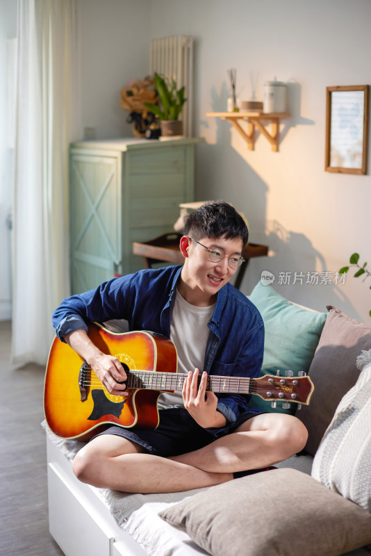 青年男人坐在沙发上弹吉他