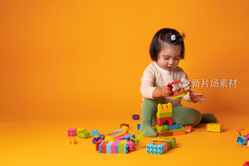 坐在黄色背景前玩积木的中国女童