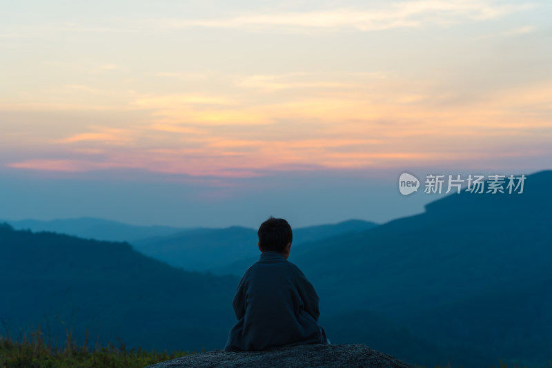 日落时坐在山上的人的后视图