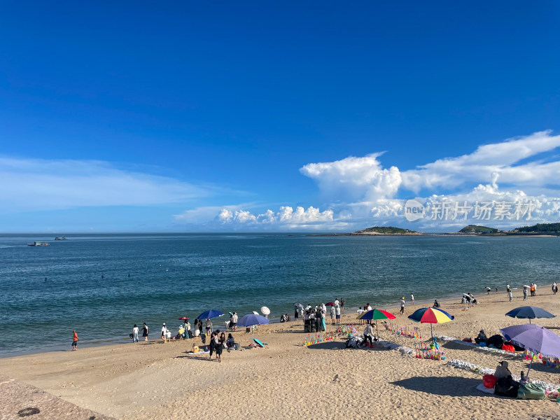 蓝天白云下热闹的海边沙滩景象