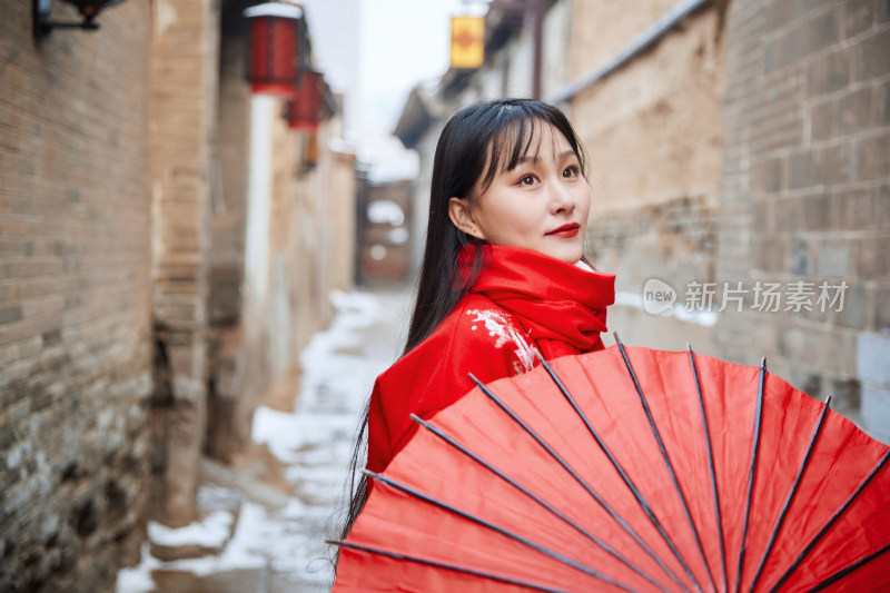 雪后在老城古巷穿着喜庆服饰的亚洲少女