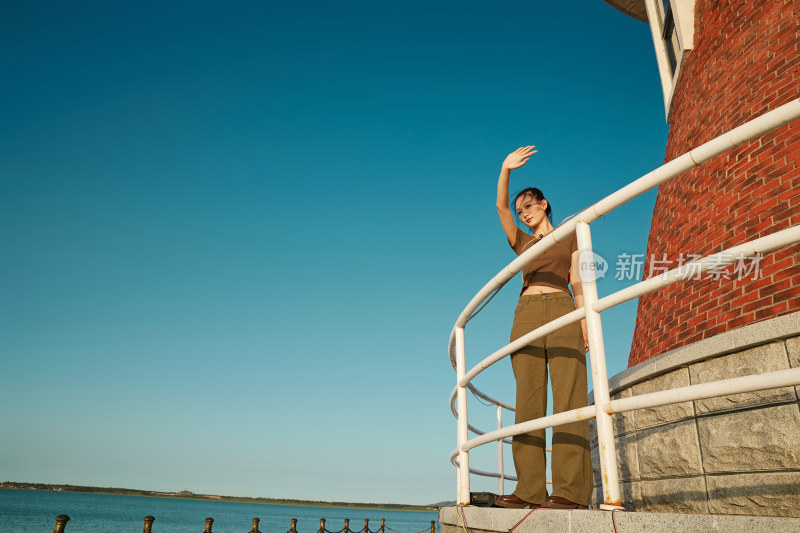 盛夏夕阳晚霞湖边码头灯塔上的少女