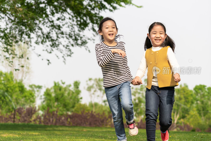 夏天两名牵手在公园草坪上奔跑中国女孩