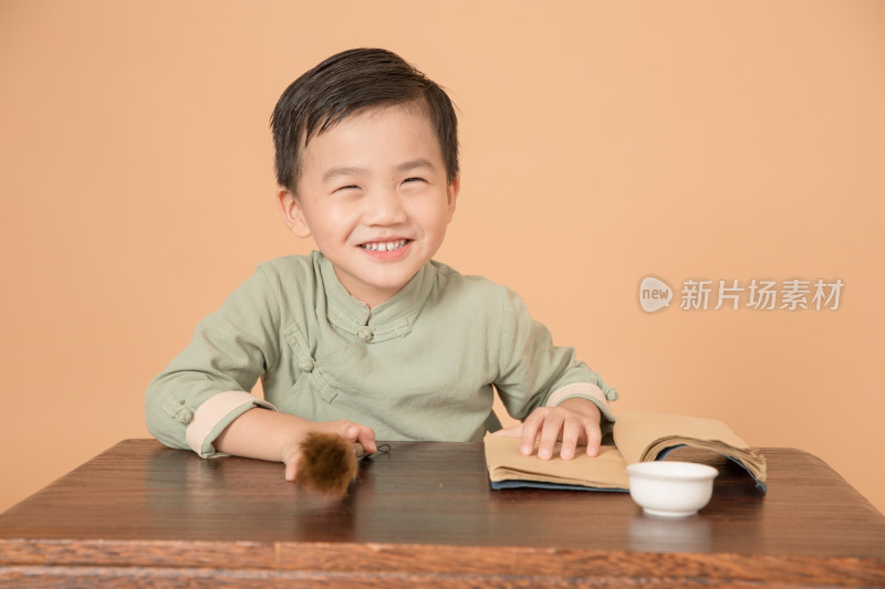 拿着毛笔坐在书桌前的中国古风小男孩