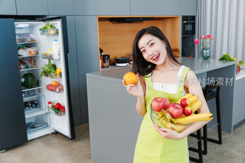 拿着水果的青年女人站在冰箱前