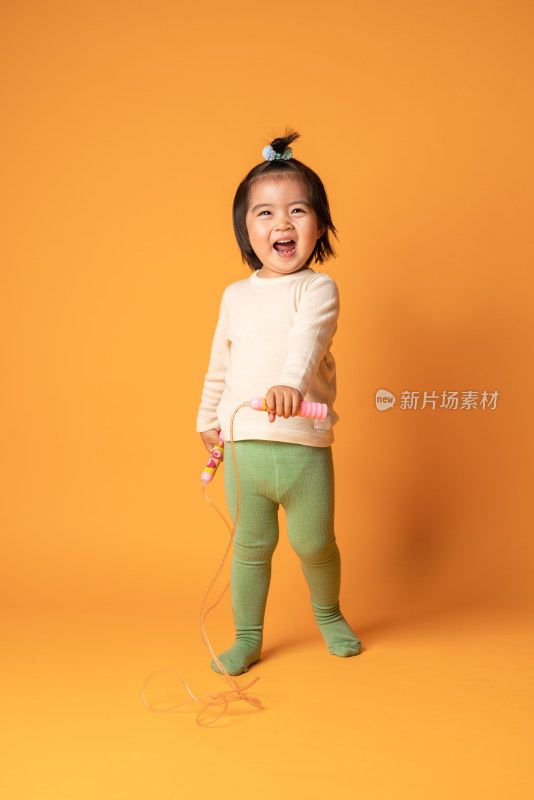 在黄色背景前玩跳绳的中国女童