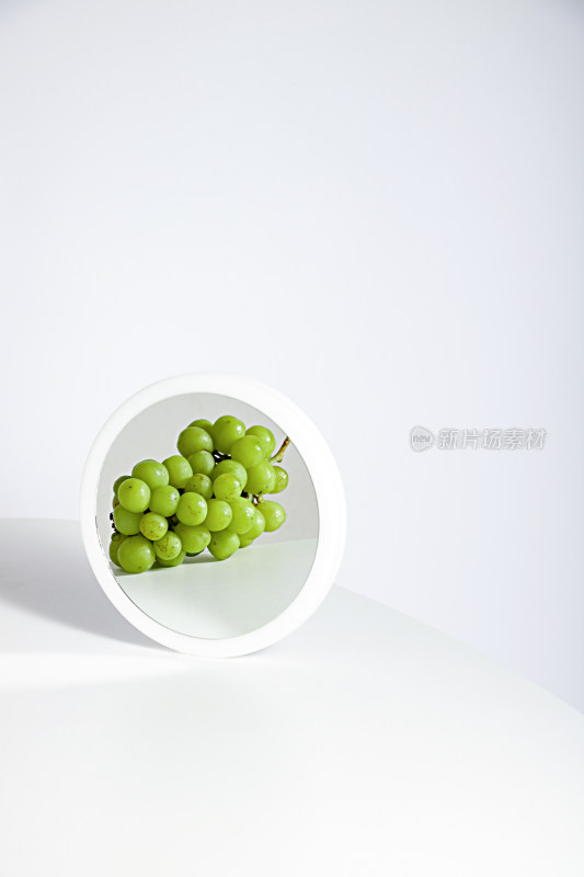 白色桌面和镜子中的新鲜水果葡萄提子