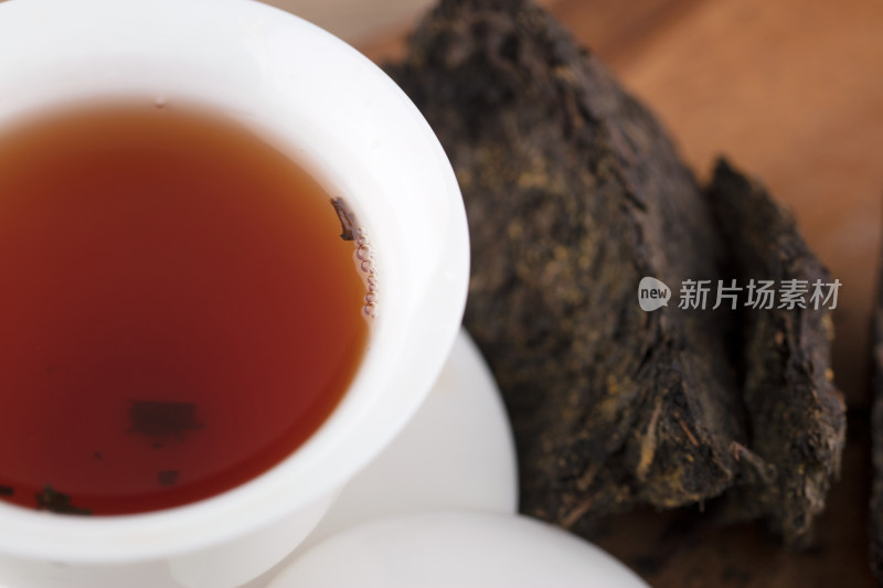 红润的茯茶茶汤在盖碗里及旁边的茶块