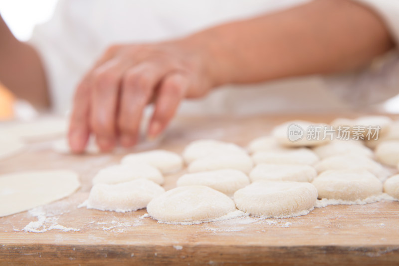 砧板上散落着小面团和背景里正在包饺子的手