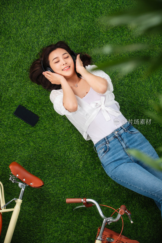躺在草地上听音乐的年轻女人