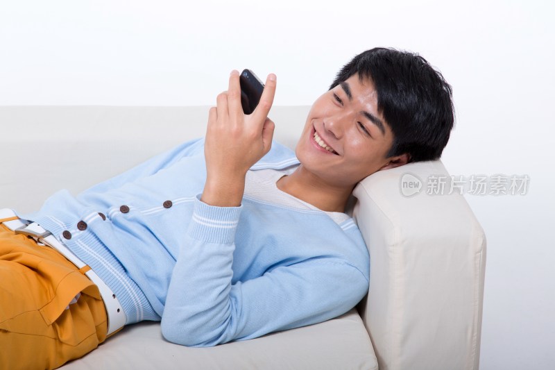 棚拍年轻男人躺在沙发打手机
