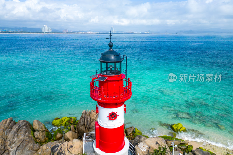 阳光下的海南三亚海岸线上礁石海浪花灯塔