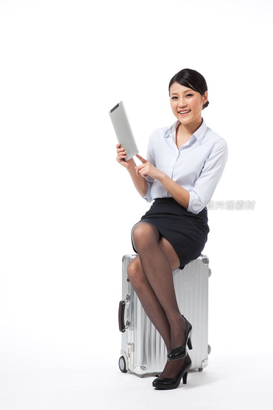 棚拍年轻商务女士坐在旅行箱上玩平板电脑